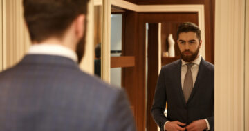 View from back of man in suit looking at the mirror while being in shop